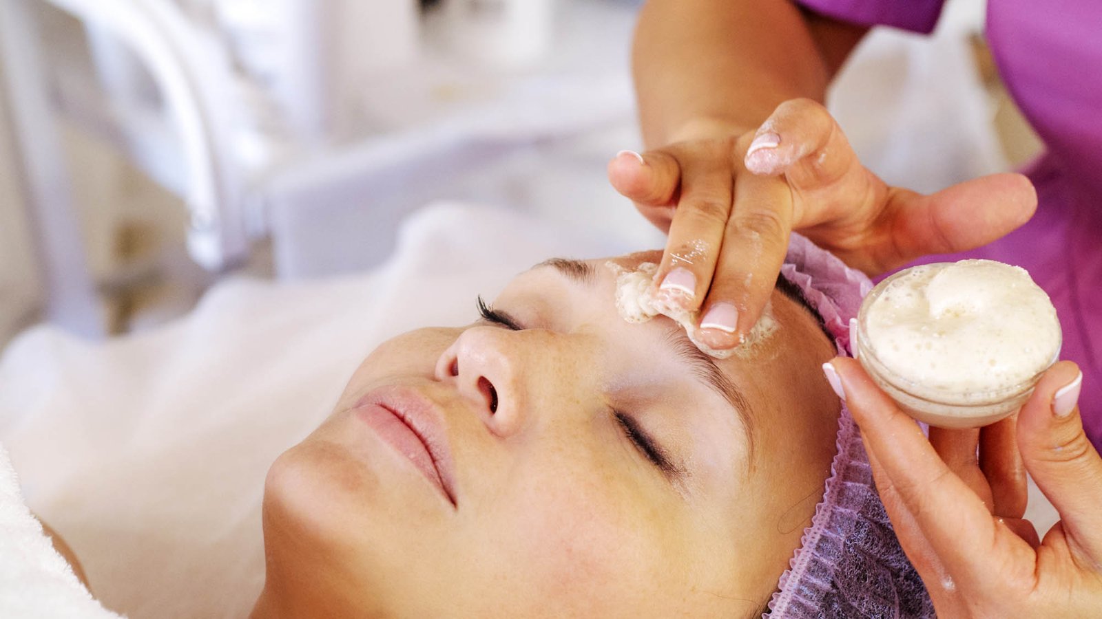 Cosmetologist applies  a moisturizing mask on female face. Woman in a spa salon on cosmetic procedures for facial care.  White woman getting beauty treatment therapy.